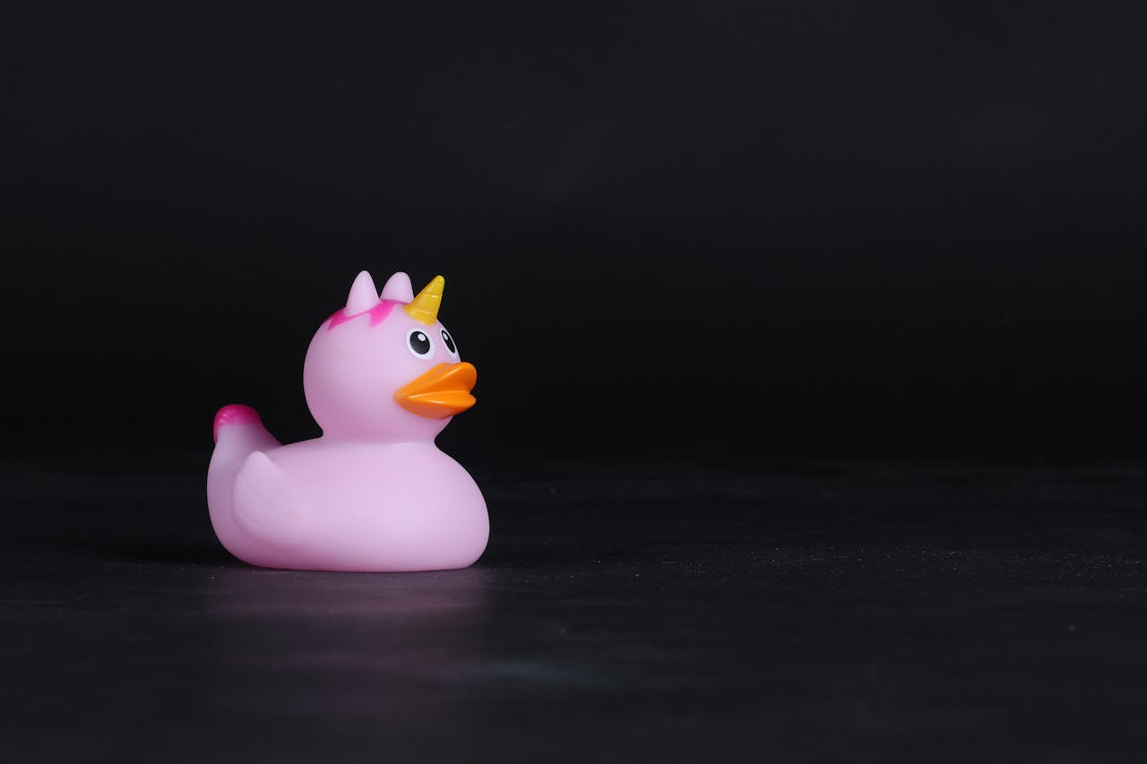 A whimsical pink rubber duck toy with unicorn horn on a dark backdrop, perfect for bath time fun.